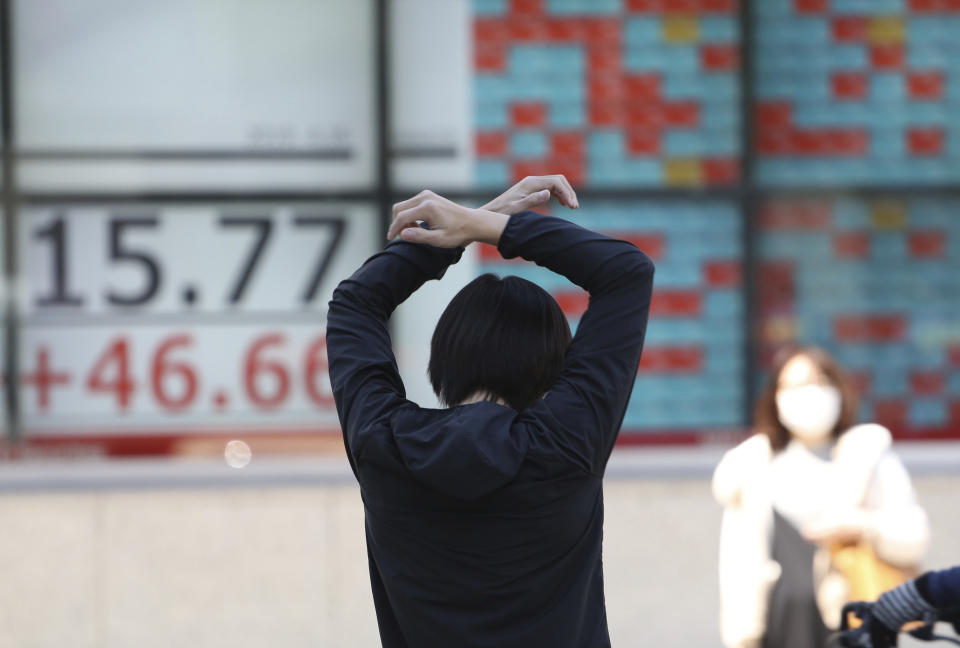 A man stretches in front of an electronic stock board of a securities firm in Tokyo, Tuesday, April 16, 2019. Shares were mixed Tuesday in Asia in mostly narrow trading in the absence of any major market-driving news.(AP Photo/Koji Sasahara)