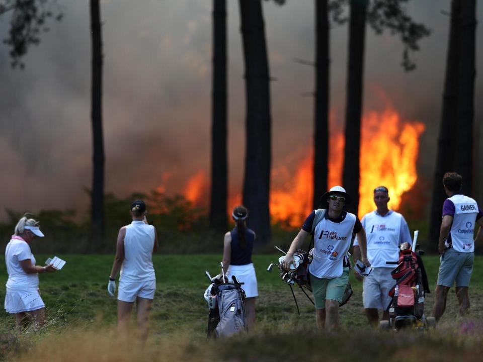 Players Sophie Powell, Cara Gainer and Gabriella Cowley and their caddies look on as a fire nears the 10th hole: Getty Images