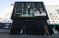 People walk past a giant screen streaming a Fendi fashion live show during the Milan's fashion week in Milan, Italy, Friday, Jan. 15, 2021. (AP Photo/Antonio Calanni)