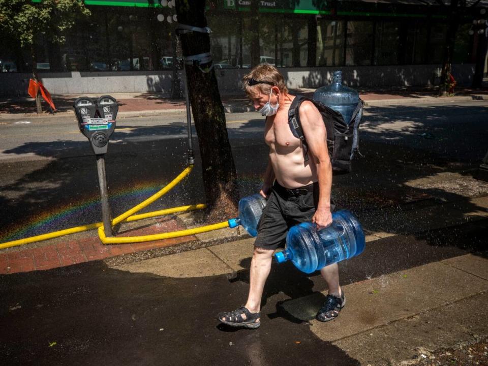 A man carrying multiple jugs of water walks through a sprinkler in Vancouver on Monday, June 29, during a record-breaking heat wave that contributed to hundreds of deaths in British Columbia. Extreme heat is just one of the climate-related health impacts the Lancet report warns will get worse as the planet warms. (Ben Nelms/CBC - image credit)