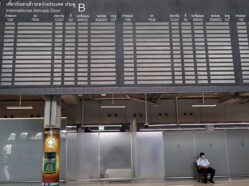 Man sits under the arrivals flight information board at Suvarnabhumi Airport in Bangkok