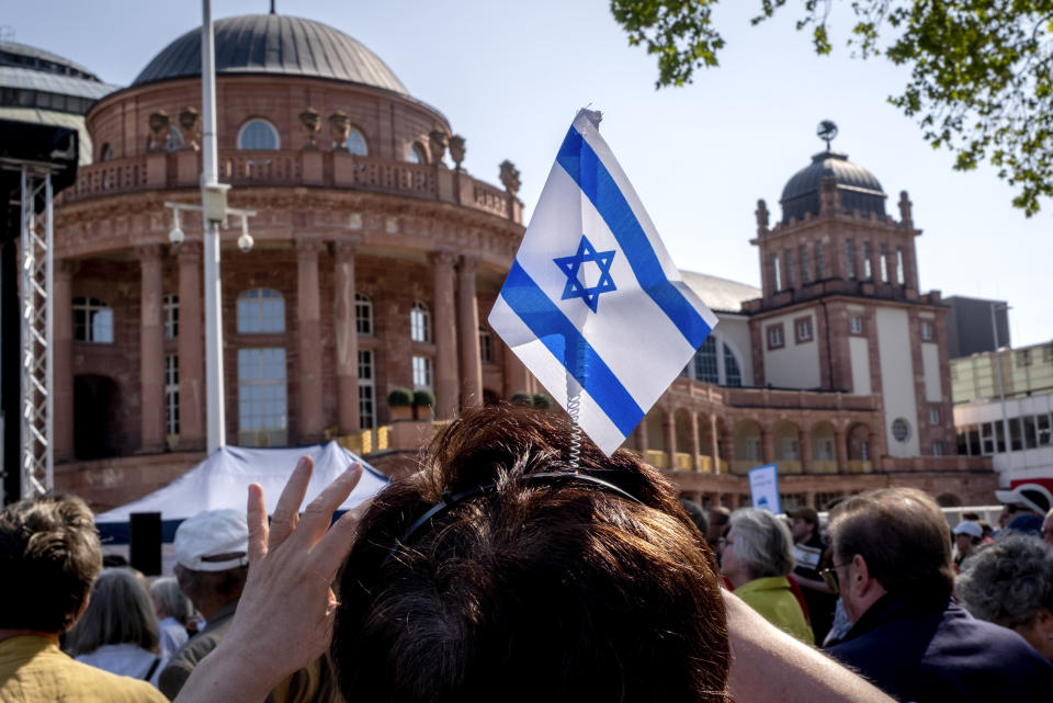 A woman wears an Israeli flag on her head as she takes part in a demonstration against a concert later the day of former Pink Floyd musician Roger Waters in the Festhalle, background, in Frankfurt, Germany, Sunday, May 28, 2023. The Festhalle was the place where in the night of broken glasses 1938 about 3000 Jewish men where gathered to deport them to concentration camps. (AP Photo/Michael Probst)