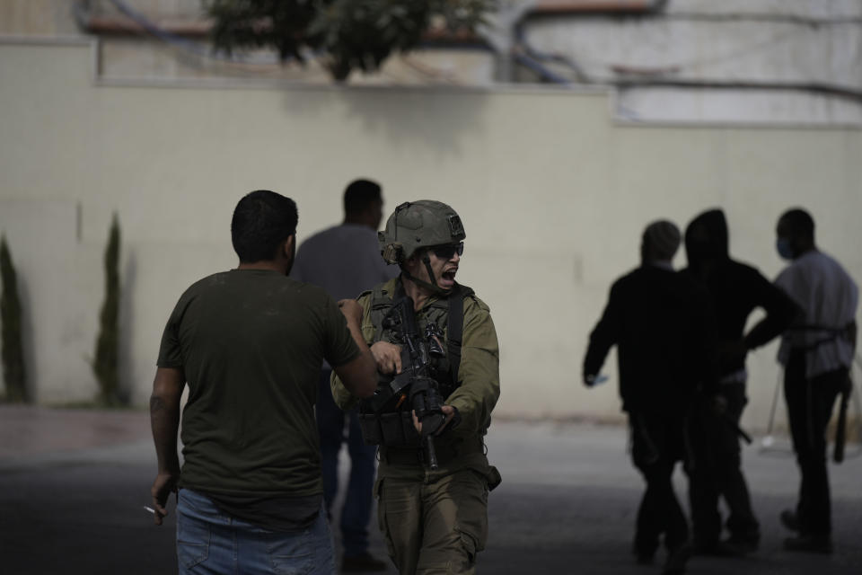 An Israeli soldier stands between a Palestinian man, left, and settlers, right, during clashes when Israeli settlers attacked Palestinians in Huwara, near the West Bank town of Nablus, Thursday, Oct. 13, 2022. (AP Photo/Majdi Mohammed)