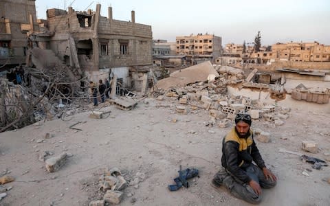 A Syrian civil defence volunteers performs ritual sunset prayers next to the site of a building that collapsed following reported regime air strikes in the rebel-held town of Arbin, in the besieged Eastern Ghouta - Credit: AFP