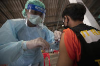 FILE - In this March 17, 2021, file photo, a health worker administers a dose of the Sinovac COVID-19 vaccine to residents of a popular market area where a new cluster of Covid 19 infections was found in Bangkok, Thailand. Now, an outbreak at nightspots in the capital Bangkok has sent new infections surging, suggesting the country may have been lulled into a false sense of security before mass vaccinations begin. (AP Photo/Sakchai Lalit, File)