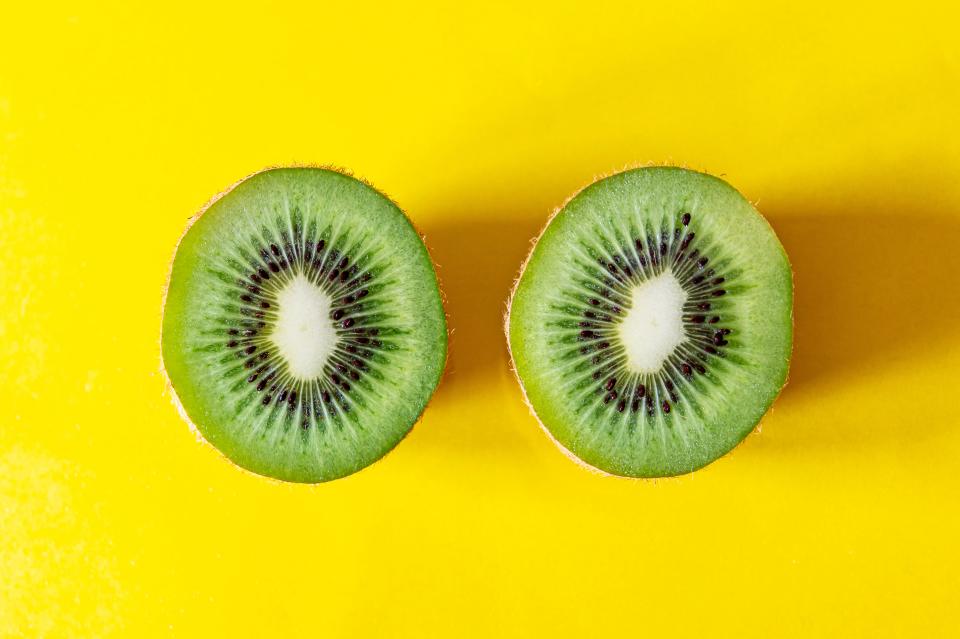 Two kiwi halves side-by-side on a bright yellow background. Copy space available.Closeup image of fresh colorful kiwi fruit cut in half on a yellow background in kitchen