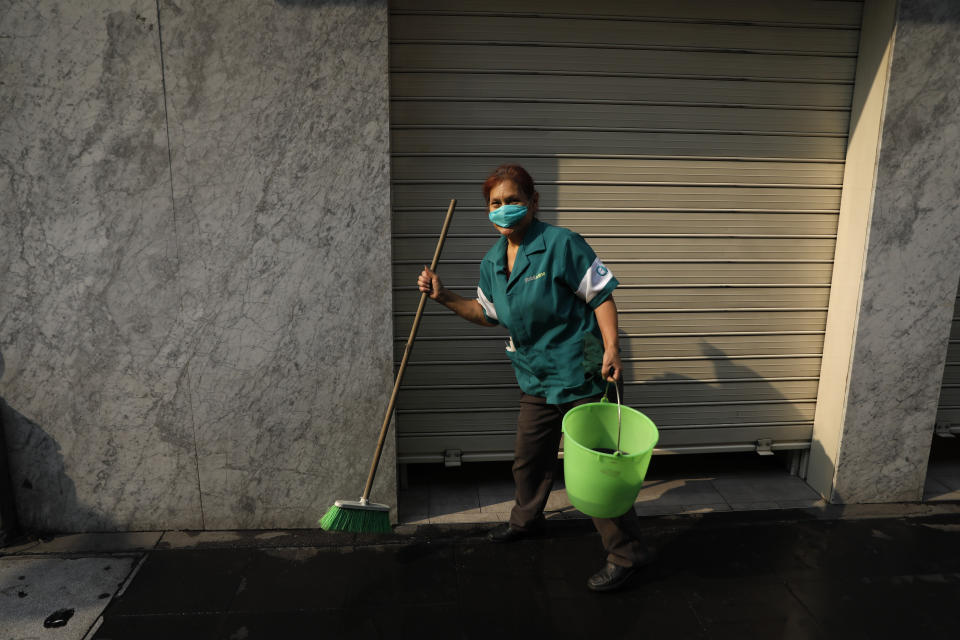 Maria Del Carmen Pineda Gomez, who says she is suffering from a respiratory infection that began three days earlier, wears a mask to protect herself against air pollution as she cleans a storefront on pedestrian Madero Street in the historic center of Mexico City, Thursday, May 16, 2019. A siege of air pollution blanketing the capital has led to school closures and the cancellation of professional sporting events.(AP Photo/Rebecca Blackwell)