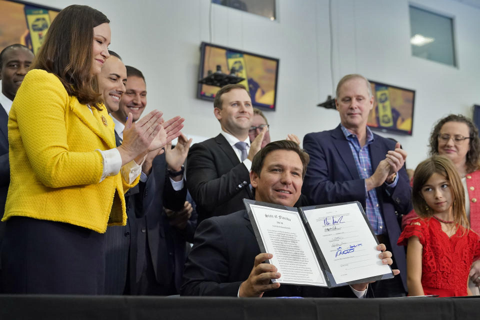 DeSantis, seated in front of a dozen supporters, holds up a signed bill.