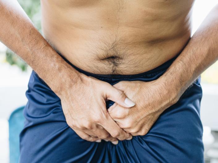 Man with hands in front of penis due to pain.