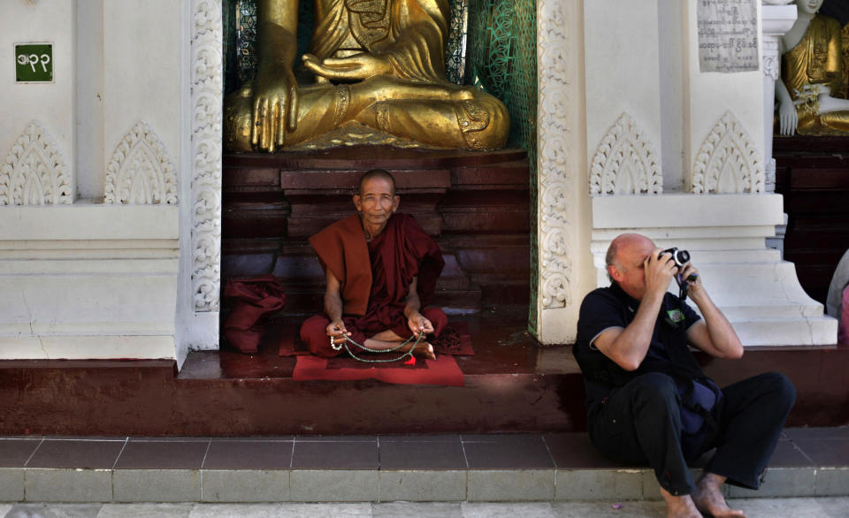 In this photo taken Feb. 21, 2012, a Myanmar Buddhist monk sits as a foreign tourist takes pictures of Shwedagon Pagoda, a famous landmark of Myanmar, in Yangon, Myanmar. Now that Myanmar is opening to the outside world, good luck getting a room. Travelers and eager investors are pouring in to explore one of Asia's most untouched countries, filling hotels to capacity, doubling room rates and spilling flight reservations onto waitlists. (AP Photo/Altaf Qadri)