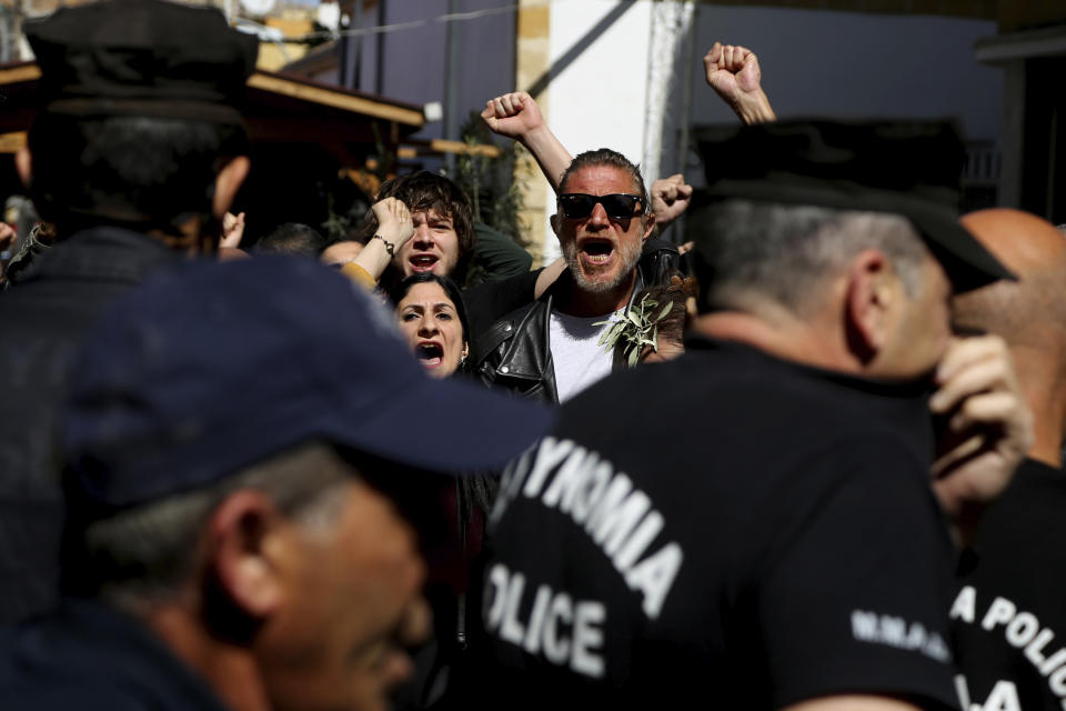 Turkish Cypriot demonstrators behind the Greek Cypriots riots police, shout slogans during a protest against a closed crossing point in the ethnically divided capital Nicosia, Cyprus, Saturday, March 7, 2020. Demonstrators staged another protest against a decision by the Cyprus government to temporarily shut four of nine crossing points along a United Nations controlled buffer zone that separates the south from the breakaway Turkish Cypriot north. The Cypriot government says it shut the crossing points to better check for potential coronavirus carriers. (AP Photo/Petros Karadjias)
