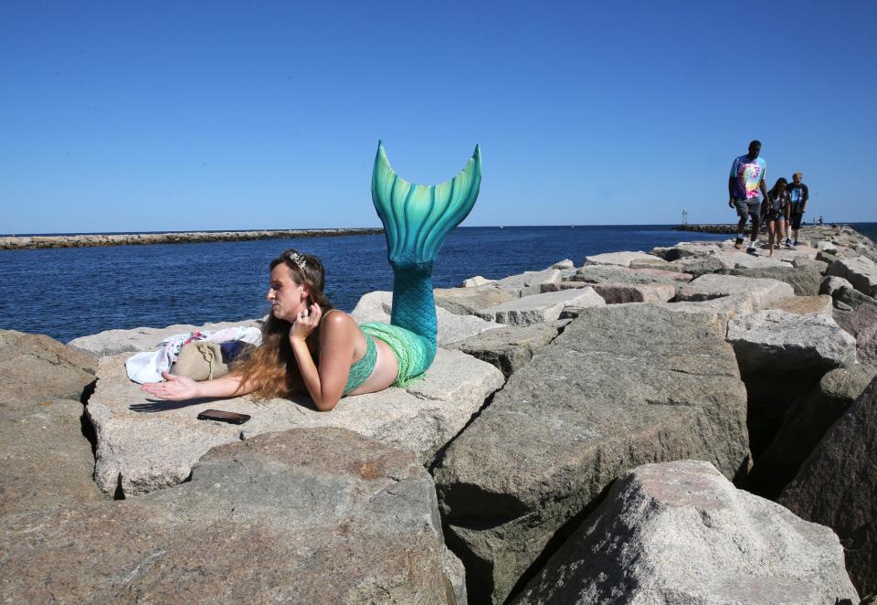 Mermaid Lavinia lies on the jetty rocks while a reporter interviews her at Wells Beach Aug. 23, 2023.