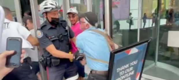 Toronto police, mall security are seen grappling with an anti-vaccine protester outside the Eaton Centre on Sept. 25. Police arrested two people as a result, charging them with assault. (Caryma Sa'd/Twitter - image credit)