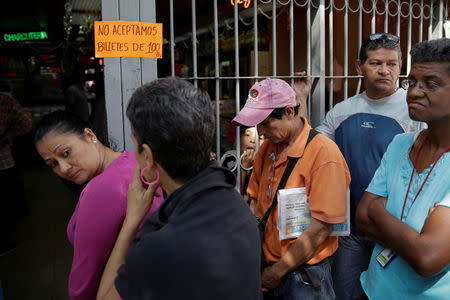 People queue to deposit their 100 bolivar notes, near Venezuela's Central Bank in Caracas, Venezuela December 16, 2016. The placard reads: "We do not accept 100 bolivar notes." REUTERS/Marco Bello