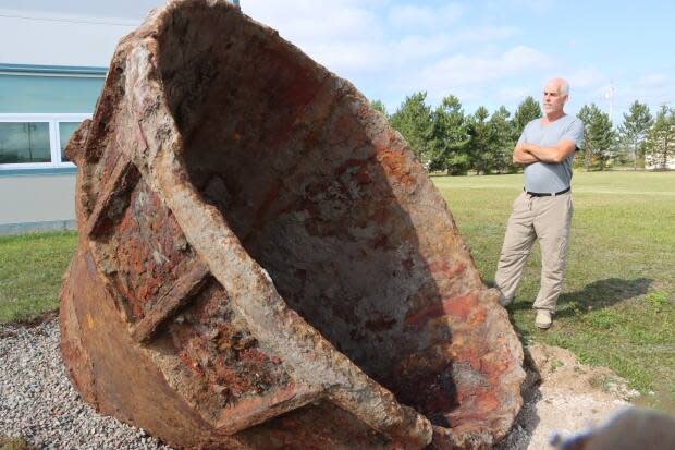 Doug Milburn stands in front of a huge, corroded metal ladle that was used in Sydney steelmaking.  (Erin Pottie/CBC - image credit)