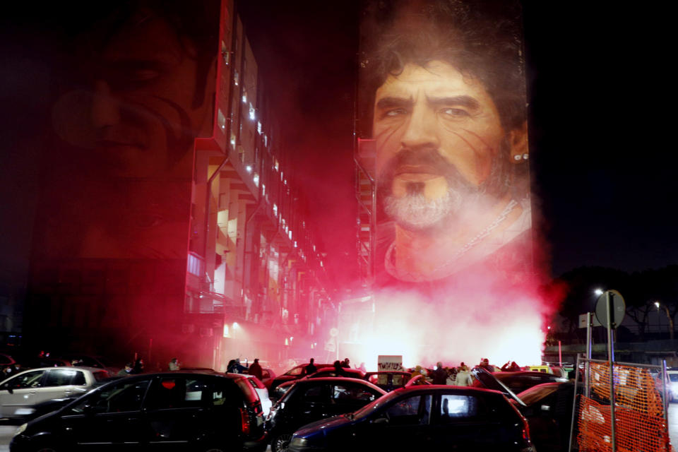People light flares as they gather under a mural depicting soccer legend Diego Maradona, in Naples, Italy, Wednesday, Nov. 25, 2020. Diego Maradona has died. The Argentine soccer great was among the best players ever and who led his country to the 1986 World Cup title before later struggling with cocaine use and obesity. He was 60. (Fabio Sasso/LaPresse via AP)