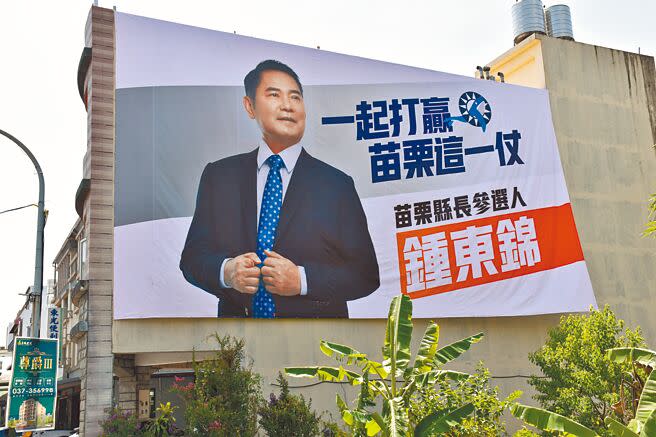 堅持參選到底的苗栗縣議長鍾東錦刻意將參選看板懸掛在國民黨苗栗縣黨部對面建築外牆上，與謝福弘看板相鄰相對，較勁意味濃厚。（謝明俊攝）