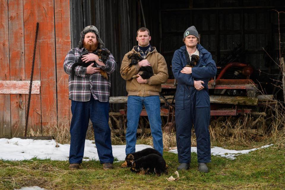 three guys holding puppies outside of a barn