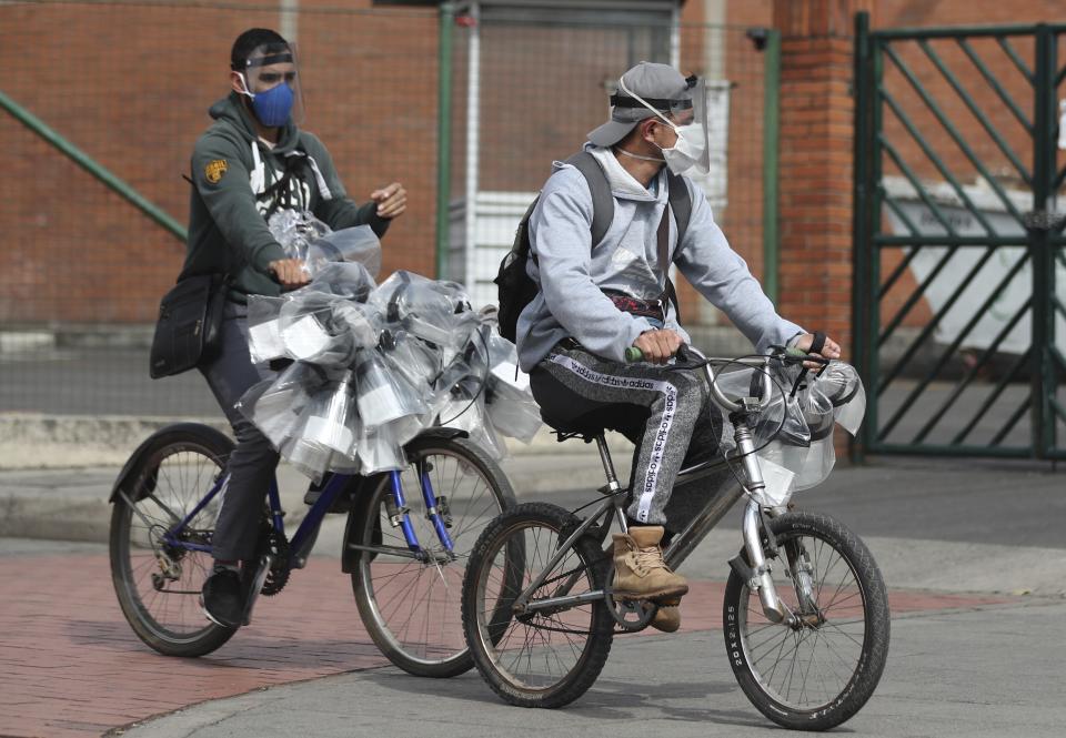 Men hawking face shields ride past on their bicycles in Bogota, Colombia, Tuesday, May 12, 2020. The mayor of Bogota ordered several areas of the capital to stay under maximum quarantine due to the high number of people infected by the new coronavirus in the area. (AP Photo/Fernando Vergara)