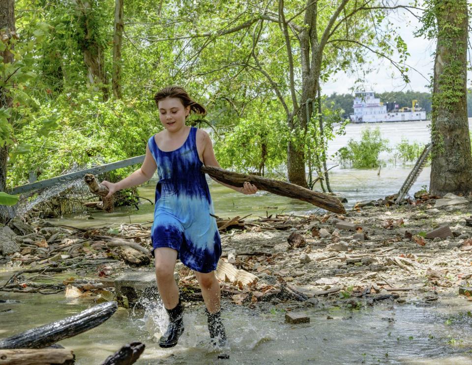 A towing vessel moves along the Mississippi River, top right, as Tallulah Campbell, 8, clears out driftwood and other debris in preparation of Tropical Storm Barry near New Orleans, La., Thursday, July 11, 2019. The area is normally a driveway at her family's home that is one of the few on land called batture on the outside of the Mississippi River levee at the border of Orleans and Jefferson Parishes. All boat traffic has been ordered to stop by Friday morning in preparation for the storm. (AP Photo/Matthew Hinton)