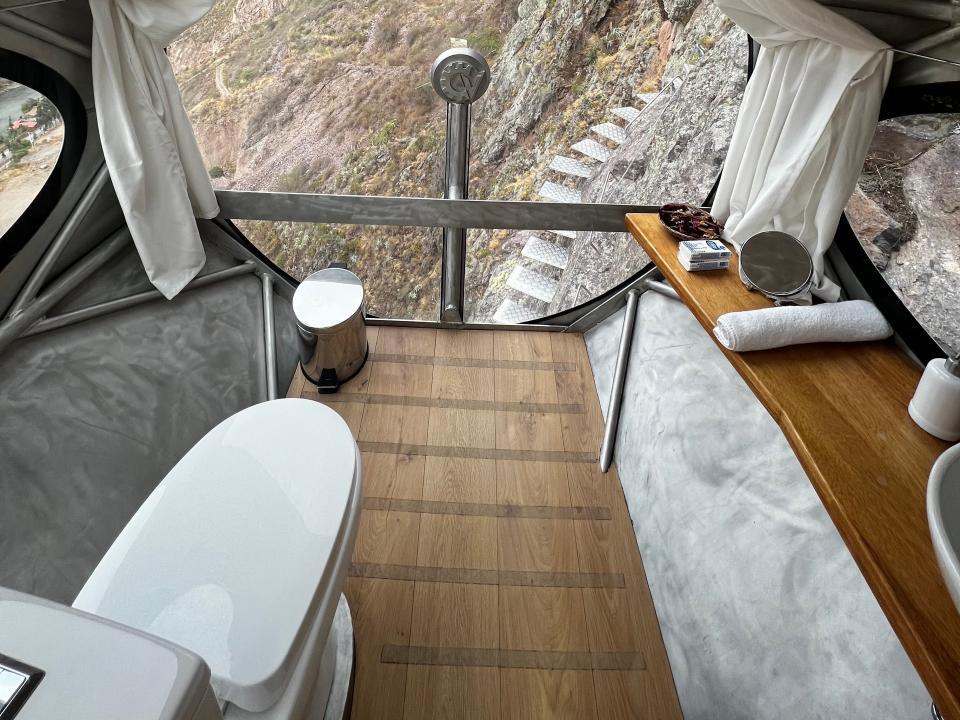 A bathroom of a hotel pod that hangs off the side of a cliff. The bathroom includes a toilet, a towel, and a small trash can.