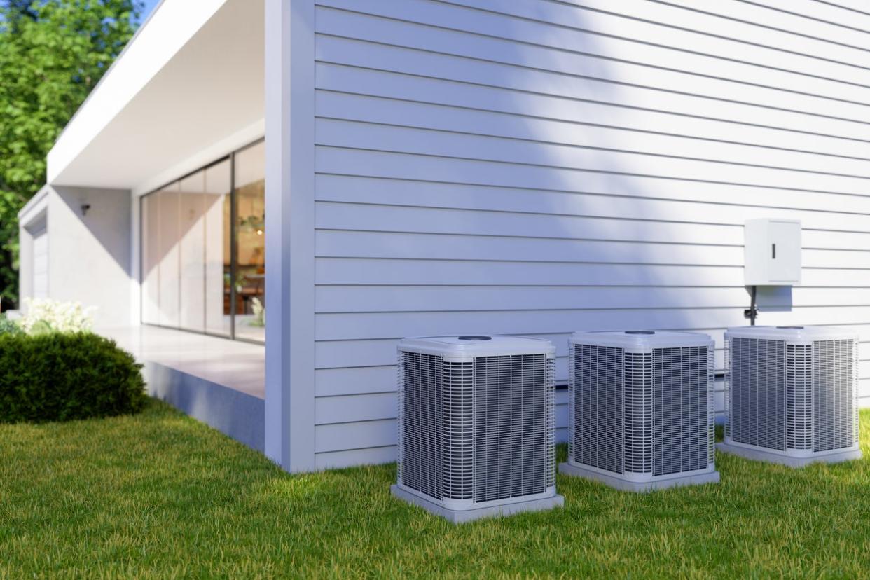 view of back of modern home with manicured lawn and three air conditioning units at the back of the house