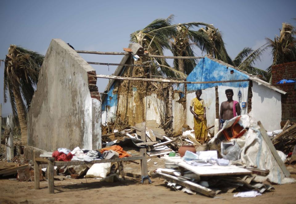 A couple stands inside their damaged house amid the debris after Cyclone Phailin hit Arjyapalli village