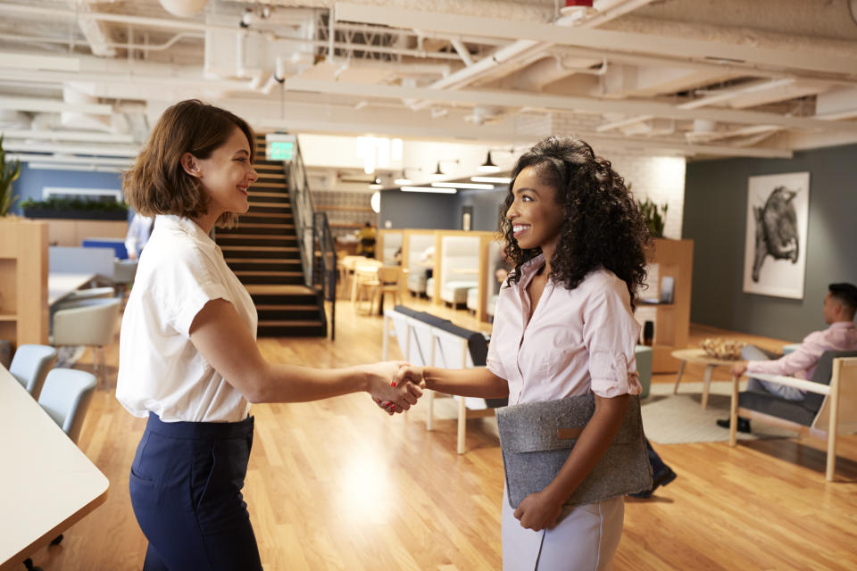 Two Businesswomen Meeting And Shaking Hands In Modern Open Plan Office