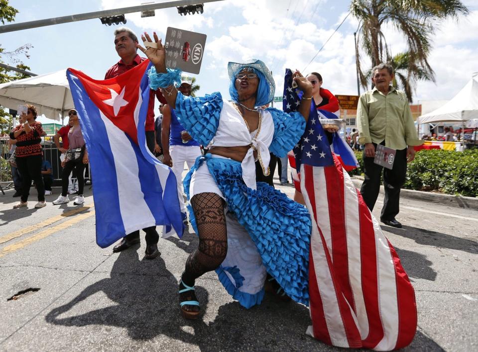 People celebrate at a festival and wave Cuban and American flags.