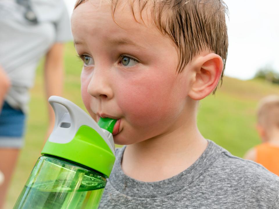 A young boy takes a break from vigorous physical exercise and plays outside, drinks water and sweats.