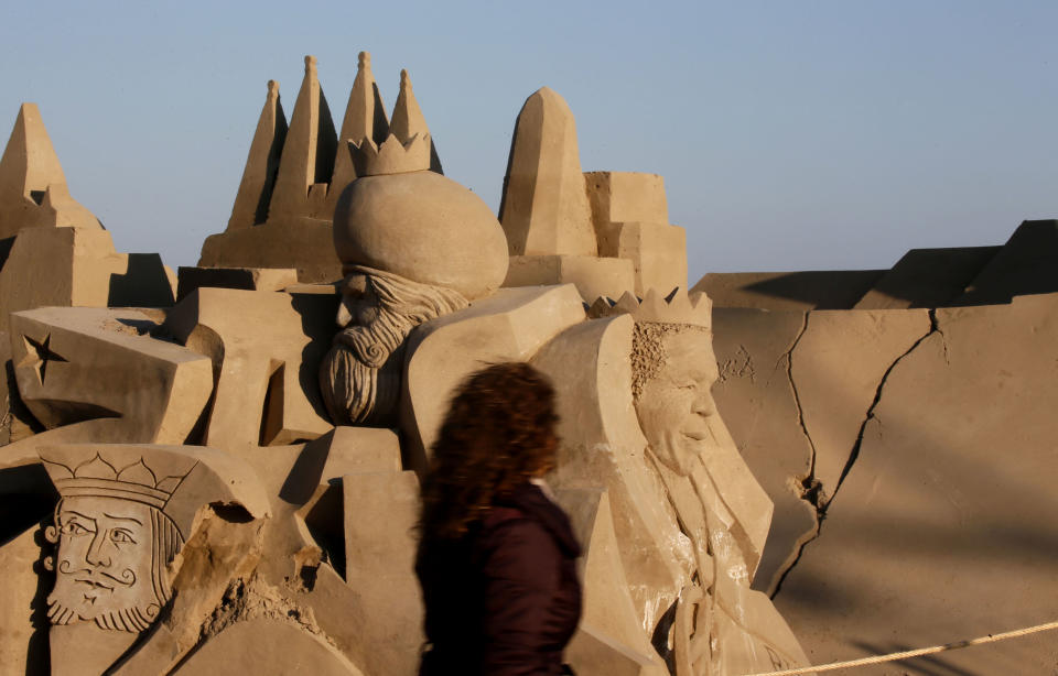 A woman walks past a nativity scene made of sand on a beach in Salou