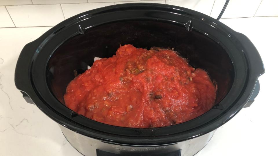 A Crock-Pot filled with ingredients, including crushed tomatoes and salsa.