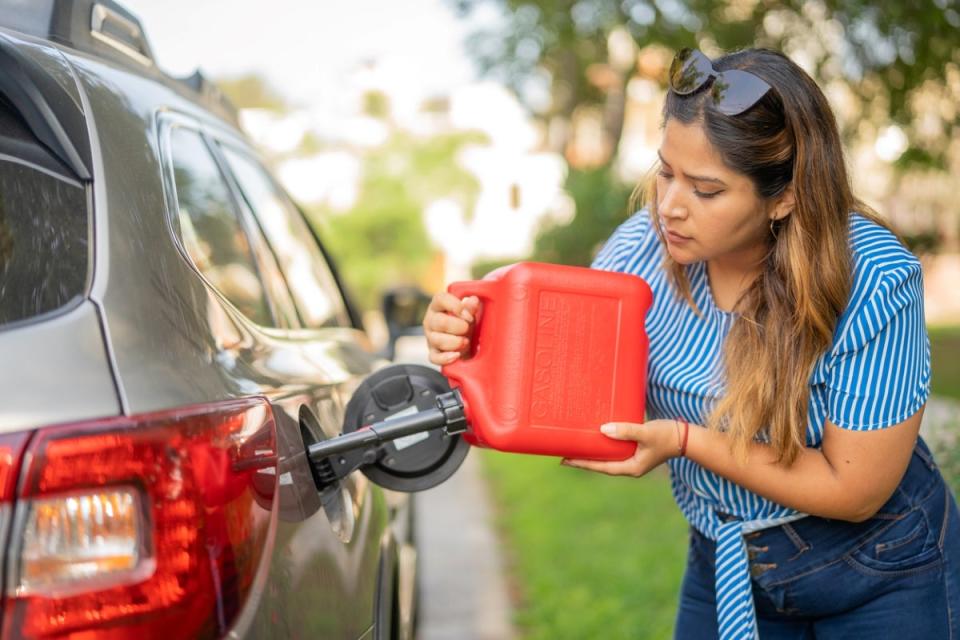 Woman pouring gas from red container in car's gas tank.
