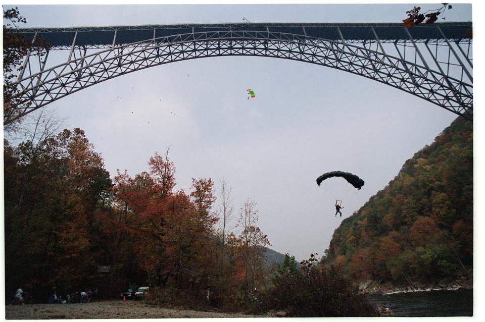 A pair of BASE jumpers fly their parachutes toward the landing zone on the banks of the New River after jumping from the New River Gorge Bridge.