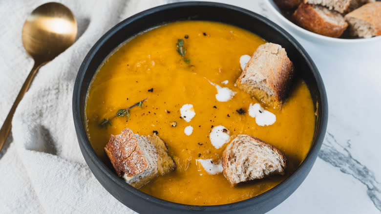 bowl of carrot soup with spoon, croutons and napkin