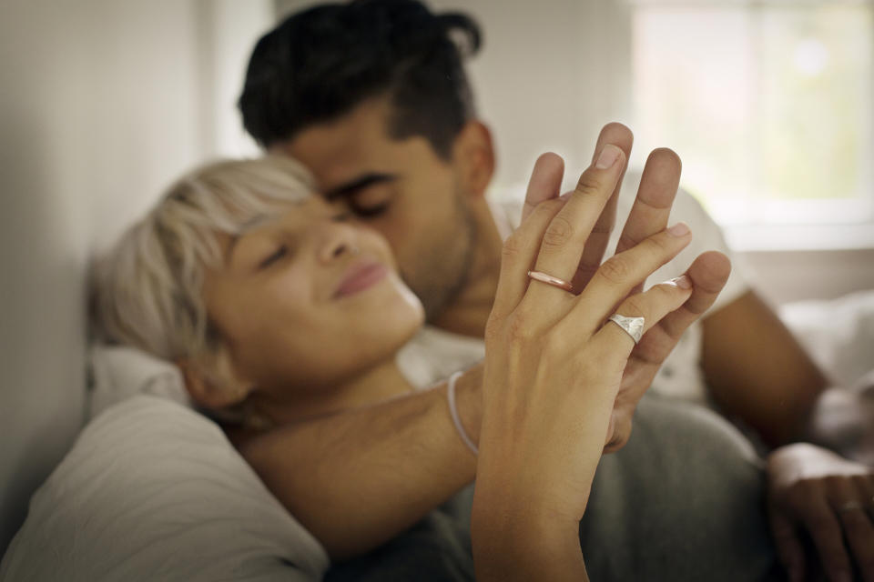 Couple embracing, woman showing off engagement ring, both appear content and affectionate
