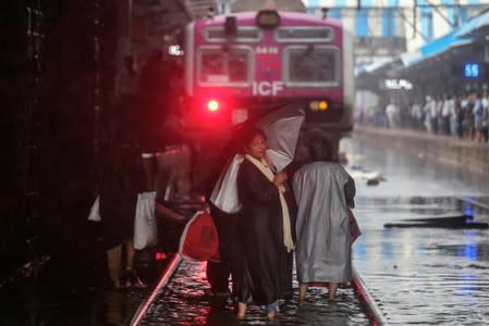 Commuters cross waterlogged railway tracks as a suburban train is seen parked at a railway station after its services were suspended during heavy monsoon rains in Mumbai