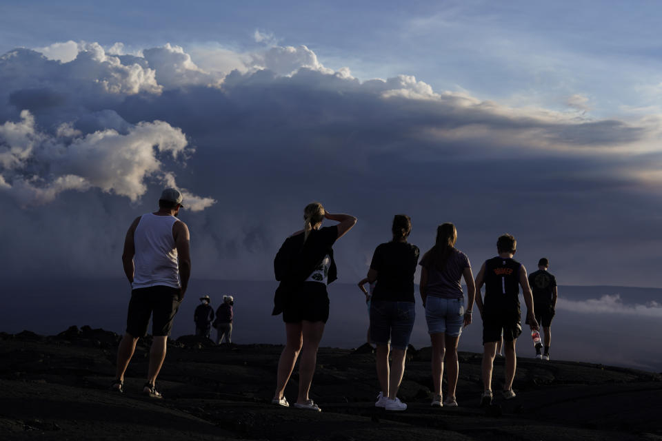 People stand on lava rock from a previous eruption near the Mauna Loa volcano as it erupts Wednesday, Nov. 30, 2022, near Hilo, Hawaii. (AP Photo/Gregory Bull)