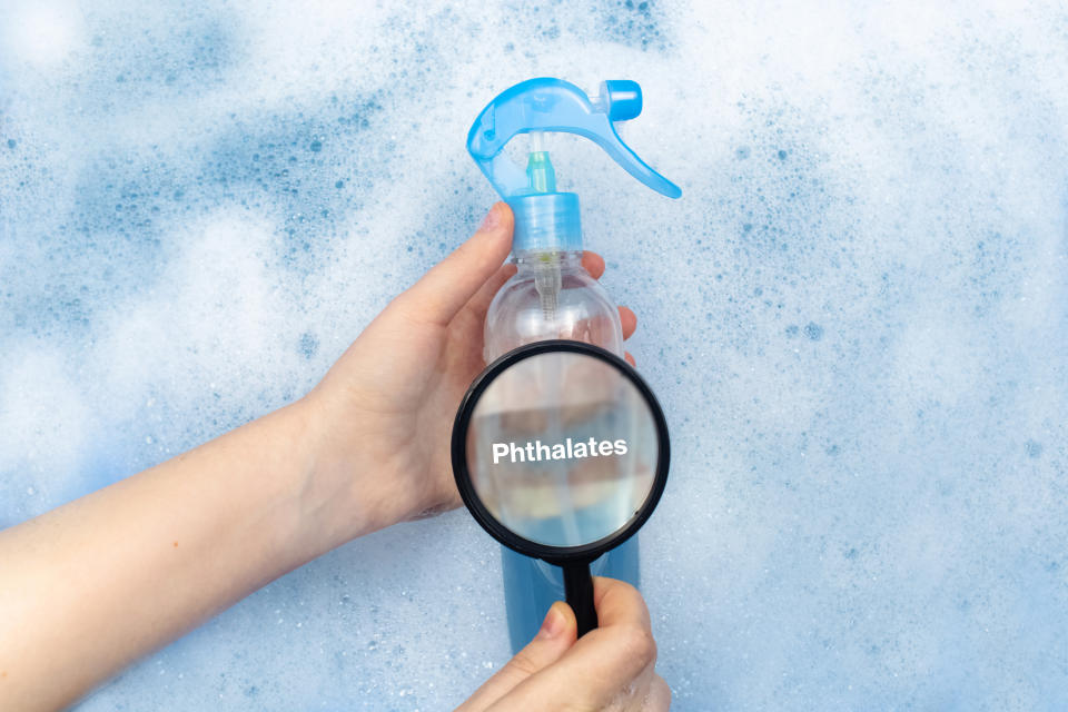 A person holding a magnifying glass up to a spray bottle, with the word 