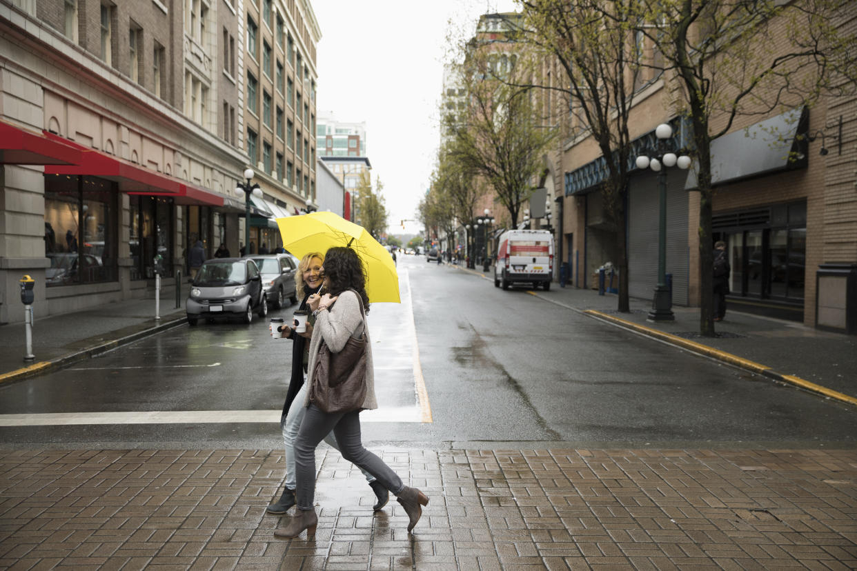 Women friends with yellow umbrella crossing city street