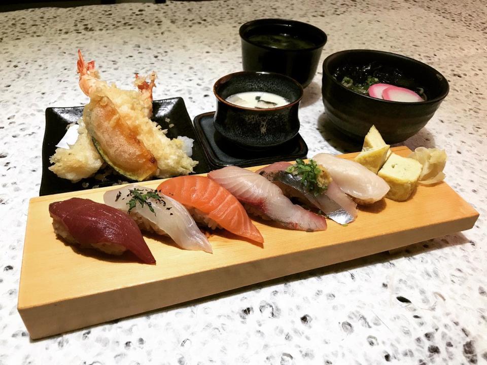 Row of unique sushis on a wooden rectangle dish together with tempura prawns, chawamushi, soup and tea