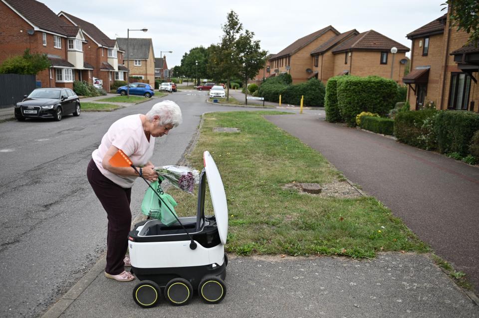 TOPSHOT - Sheila, 71, picks up a delivery from an autonomous robot called Starship delivering groceries from a nearby Co-op supermarket in Milton Keynes, England on September 20, 2021. - In a residential area in the English town of Milton Keynes small robots encased in elegant white containers roll past each other with an air of indifference, delivering shopping and meals. - To go with AFP story by Olivier DEVOS (Photo by Daniel LEAL / AFP) / To go with AFP story by Olivier DEVOS (Photo by DANIEL LEAL/AFP via Getty Images)