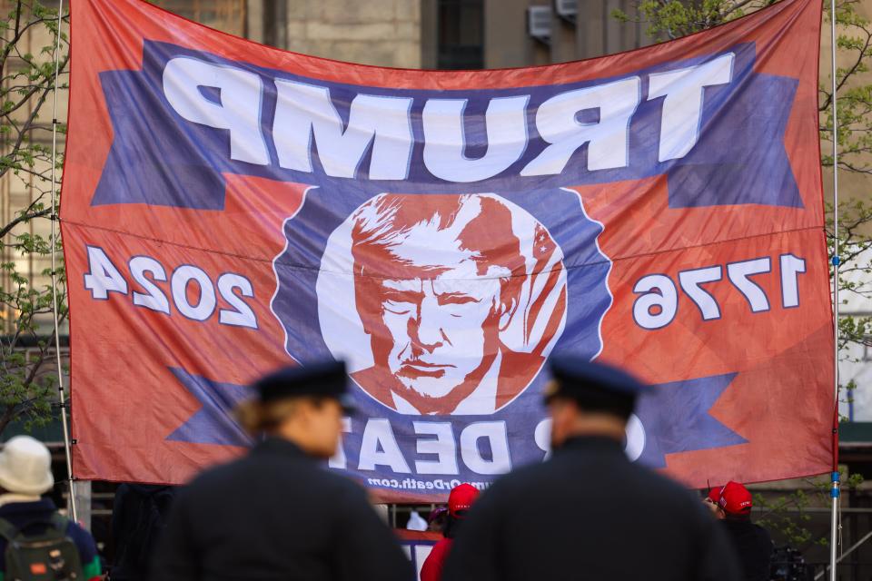 Police officers look on as supporters of former president Donald Trump hold up a flag outside of Manhattan Criminal Court, as he attends his first criminal trial on 26 April 2024 (AFP via Getty Images)
