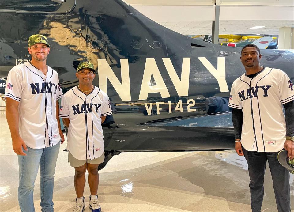 Blue Wahoos players, left-to-right, Colton Hock, Cobie Fletcher-Vance and Thomas Jones stand next to replica plane flown by baseball icon Ted Williams during his Marine training at NAS-Pensacola during World War II.