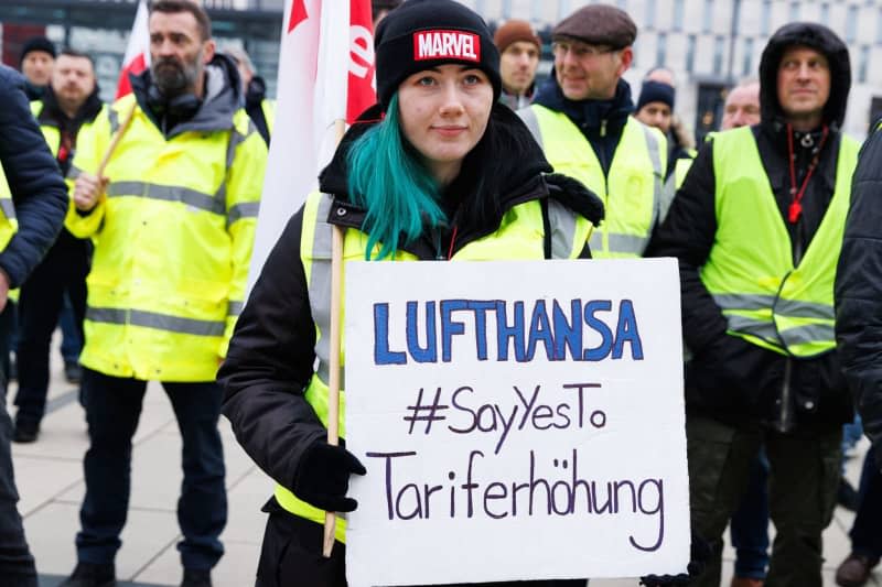 An employee holds a sign reading lufthansa #SayYesTo tariff increase at a rally of the lufthansa technik division in front of the departure hall in terminal 1 at ber airport. In the ground staff wage dispute at Germany's flagship carrier Lufthansa, technical staff began a three-day strike on Wednesday morning. Carsten Koall/dpa