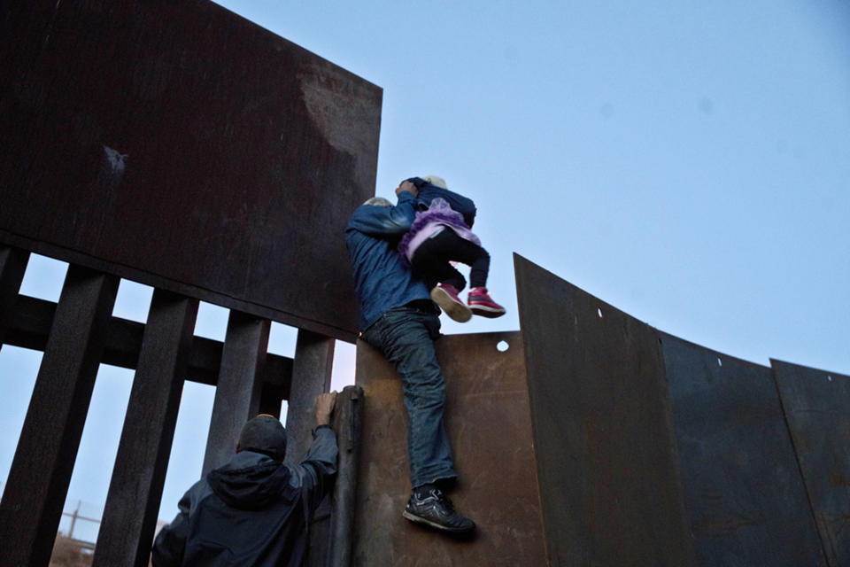 FILE - In this Dec. 2, 2018 file photo, a Honduran migrant helps a young girl cross to the American side of the border wall, in Tijuana, Mexico. A San Diego TV station says the U.S. government ran an operation to screen journalists, activists and others while investigating last year's migrant caravan from Mexico. KNSD-TV says documents leaked by a Homeland Security source show a January database listing at least 10 journalists, seven of them U.S. citizens, as warranting secondary screening at U.S. points of entry. (AP Photo/Ramon Espinosa, File)