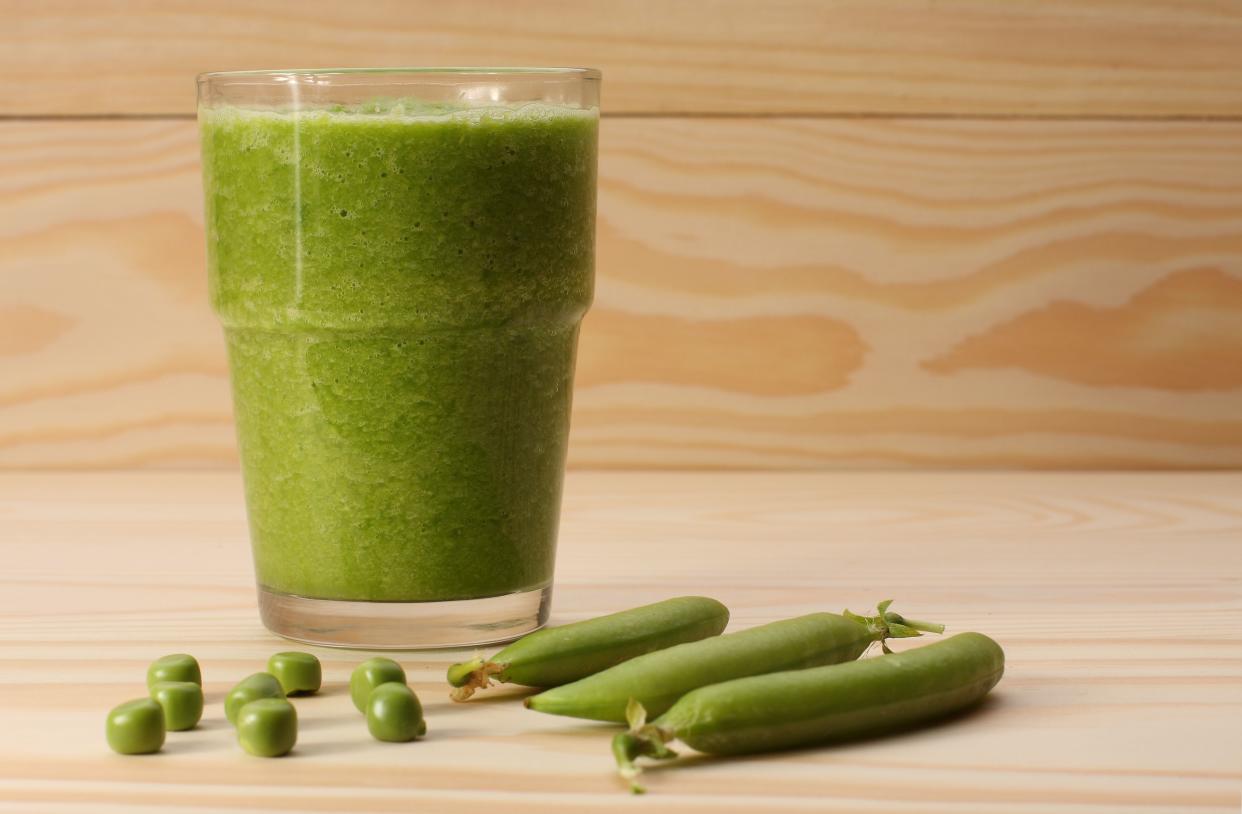 Smoothie with green peas  in a glass and pea pods  on wooden table,closeup