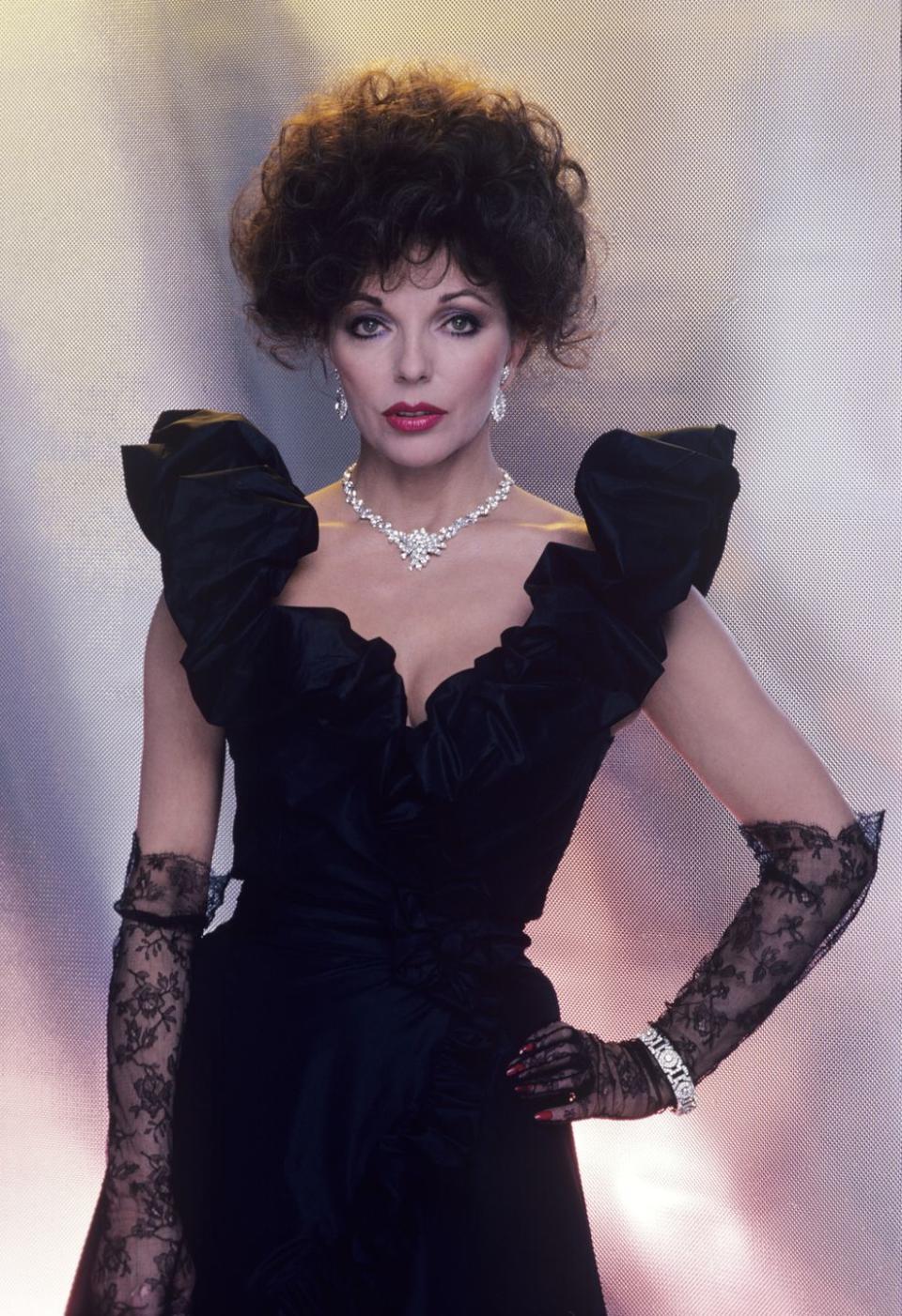 <p>Joan Collins wearing lace gloves, a ruffle-shoulder gown, and diamonds as Alexis Carrington in <em>Dynasty</em>. </p>
