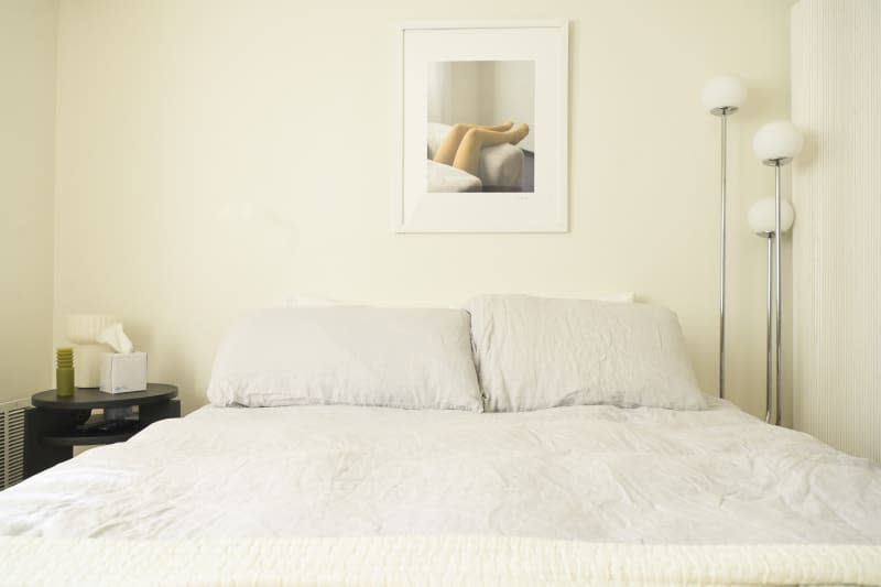 white bedroom with white bed, mid century corner lamp, and framed photo over bed