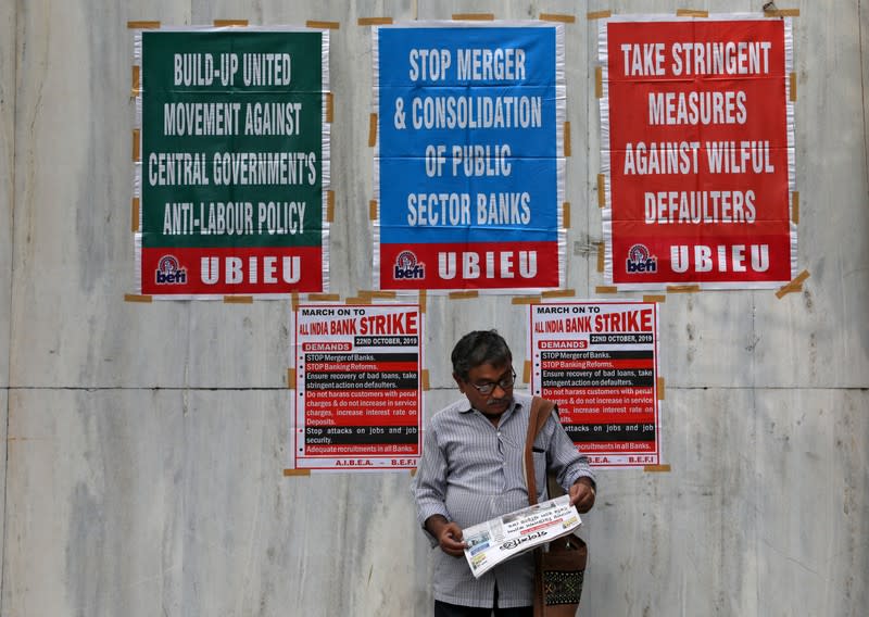 A bank employee reads a newspaper in front of the United Bank of India building during a day-long strike against mergers of several state-run banks, in Kolkata